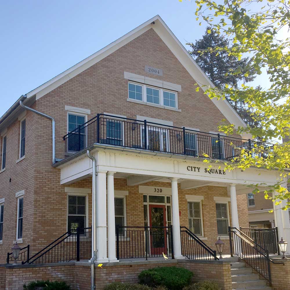 Brick building with columns and black railing on second floor