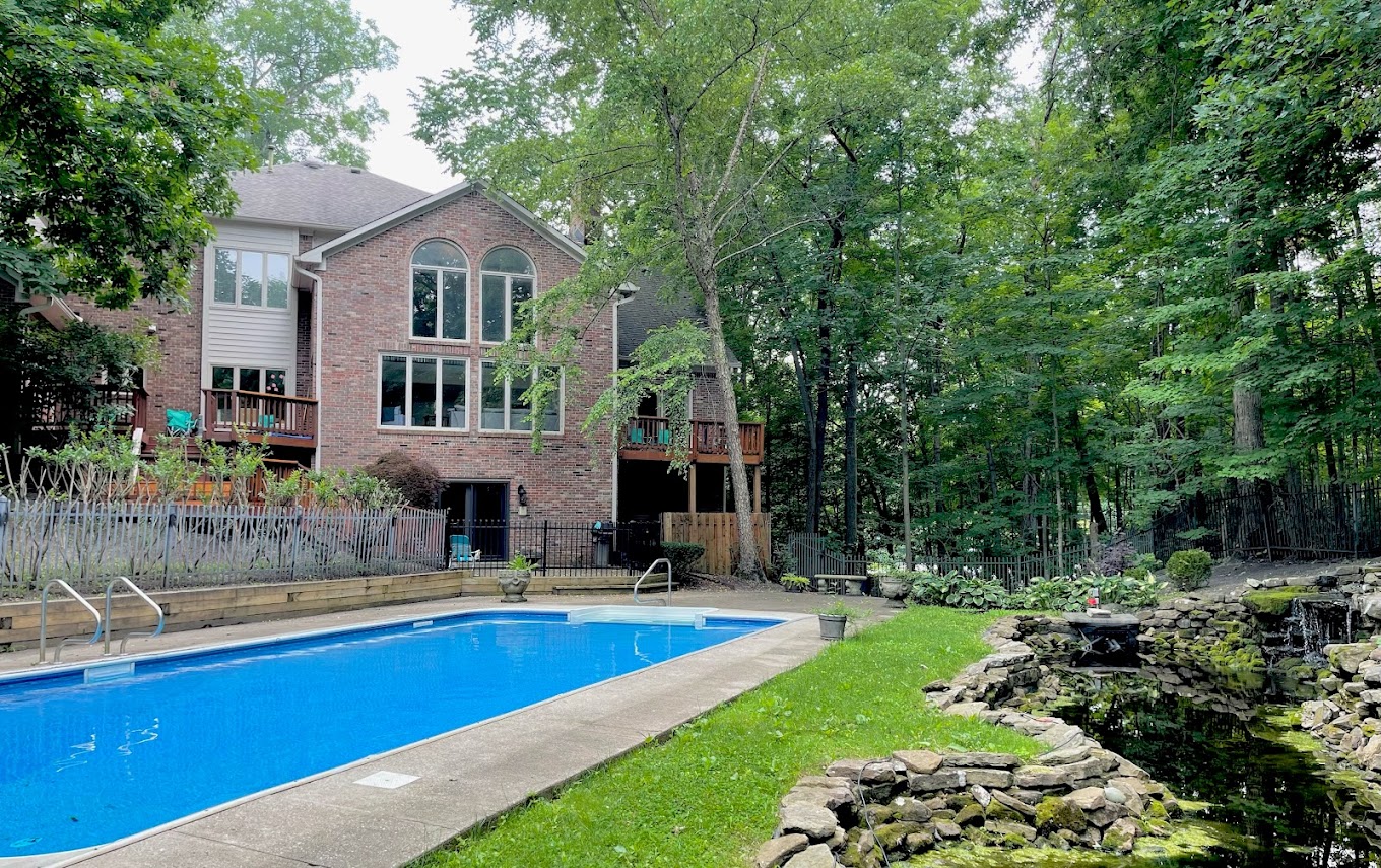 Serene backyard with a sparkling pool, lush greenery, and a tranquil pond.