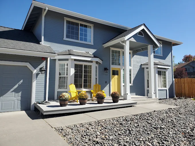 Two-story gray house with yellow door and front patio chairs