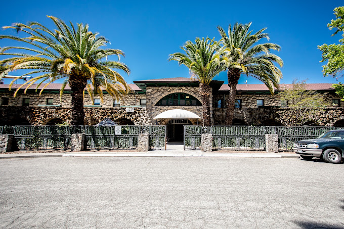 Exterior of a stone rehab facility with palm trees and gated entrance.