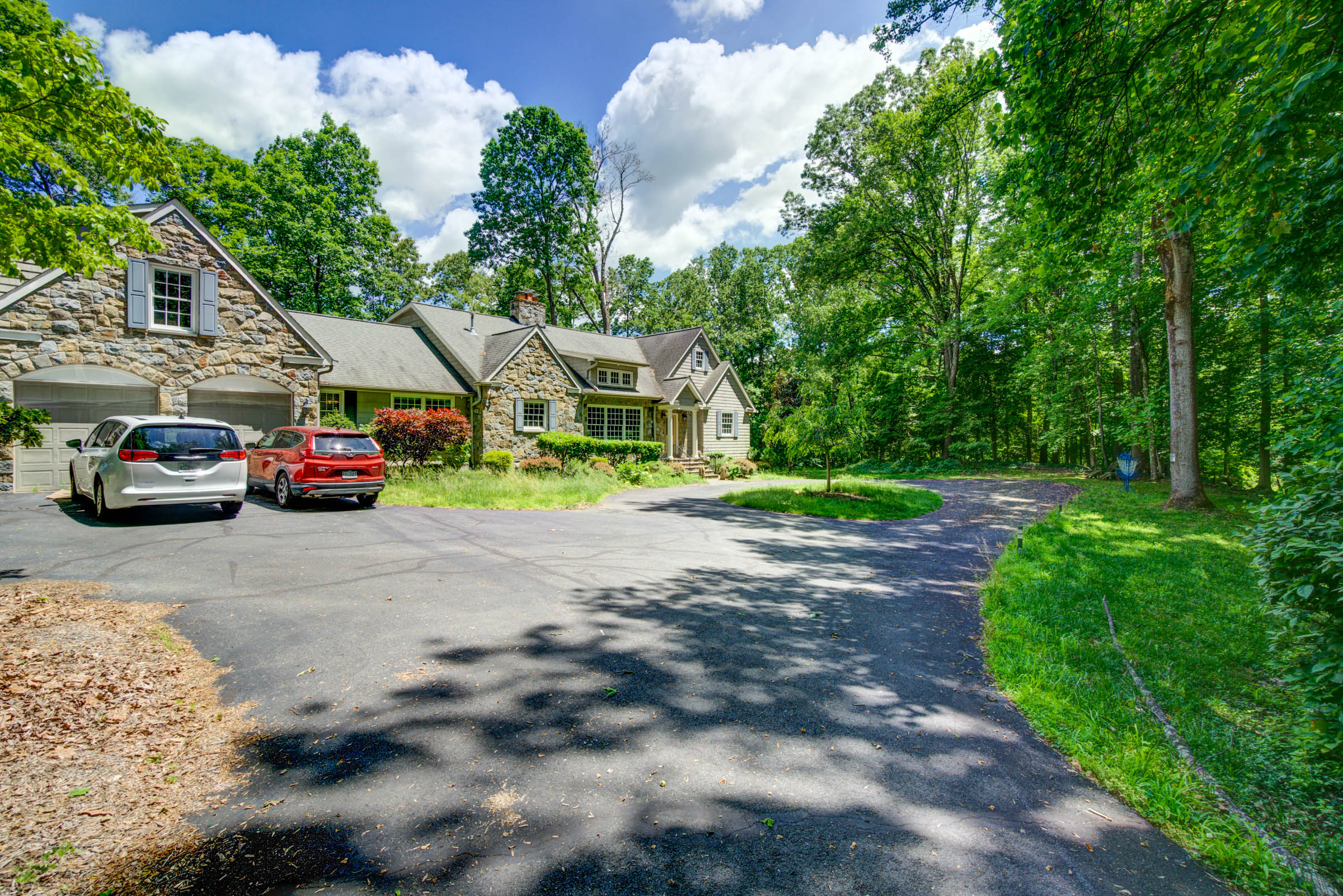 Stone home exterior with driveway and parked cars.
