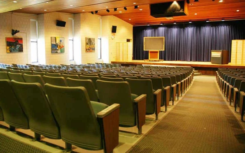 Empty auditorium with green seats facing stage and podium