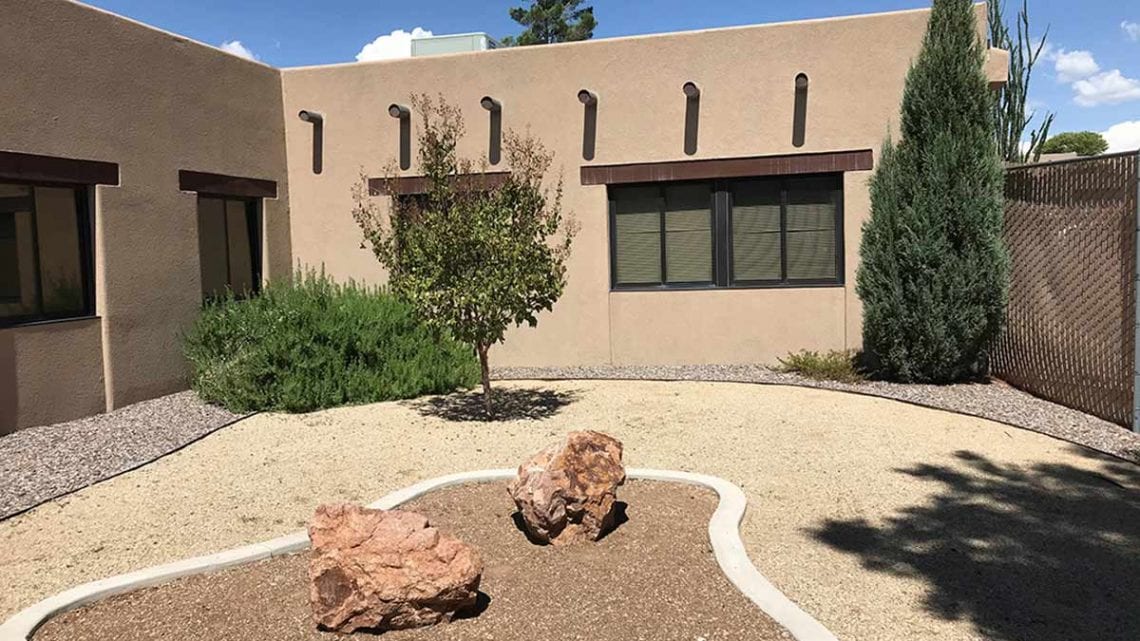 Enclosed courtyard with tree, bushes, and desert landscaping