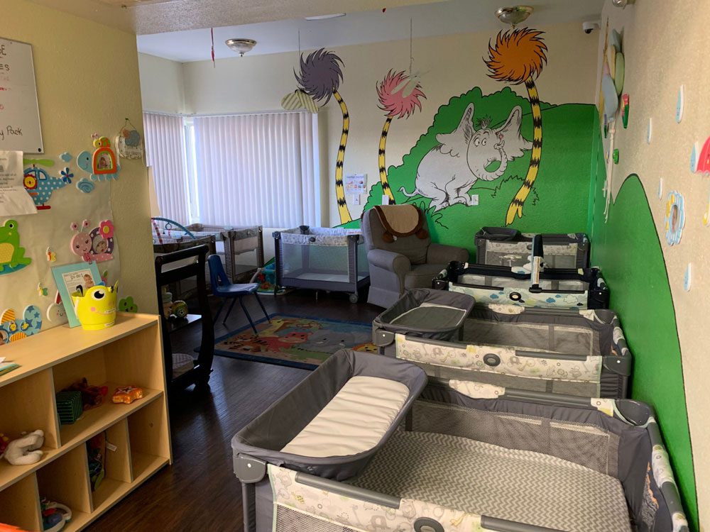 Infant room with cribs, mural art, and play area
