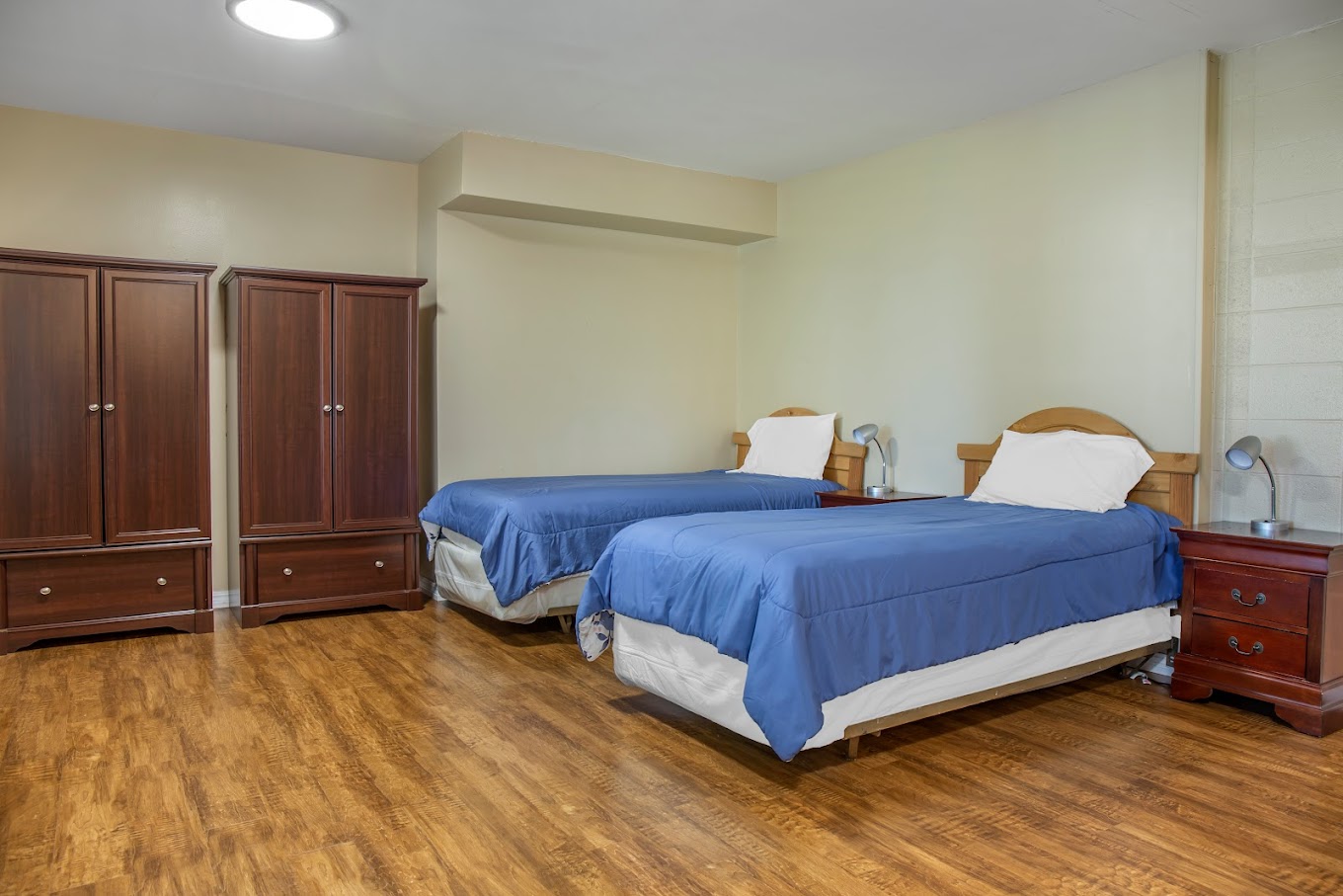 A neatly arranged bedroom with two twin beds, wooden wardrobes, and nightstands with lamps.