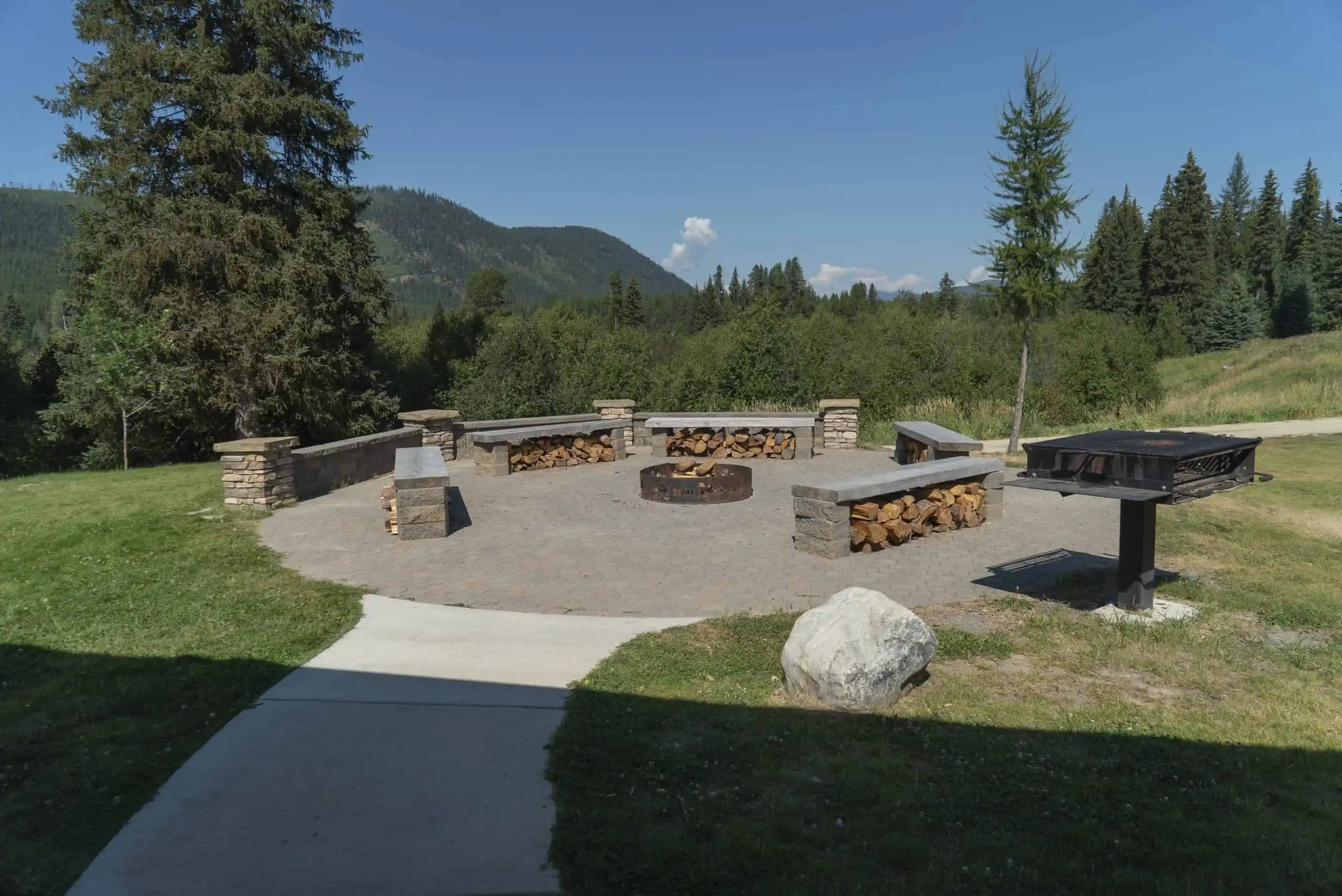 Stone fire pit with wood benches and forest backdrop