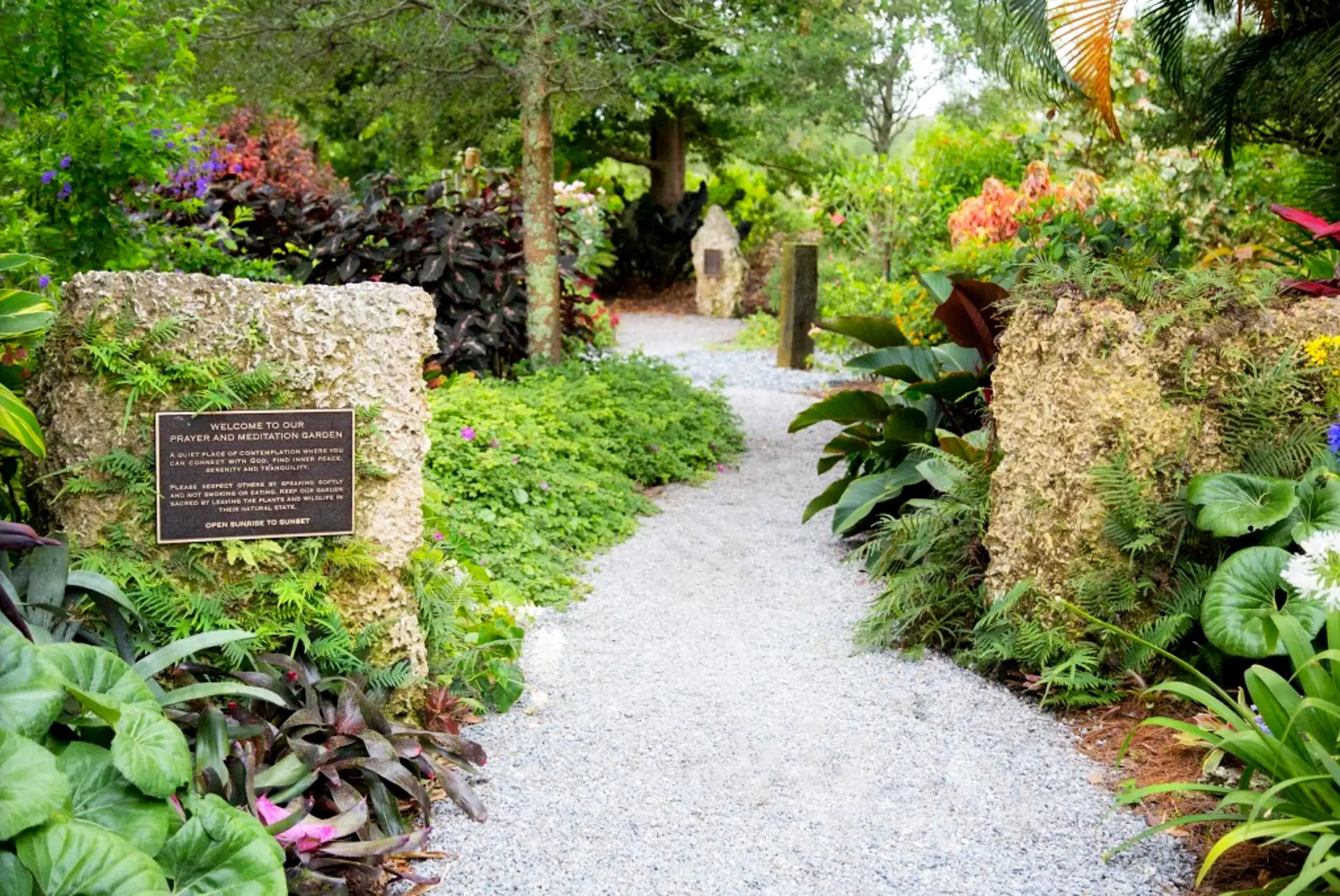 Garden path lined with plants and a welcome plaque