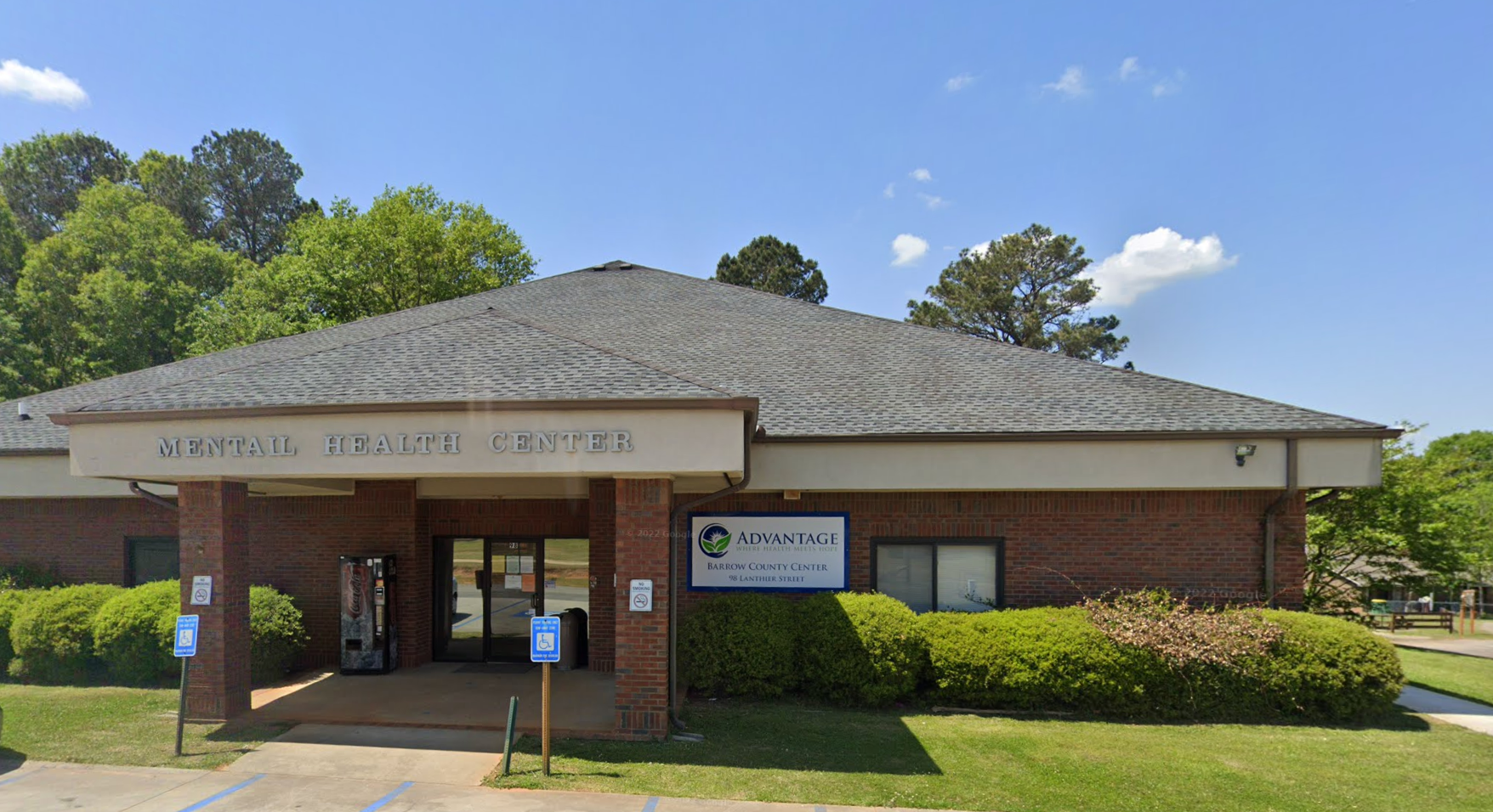 The main entrance of Barrow County Clinic with handicap parking spaces, greenery, and a vending machine near the doorway.