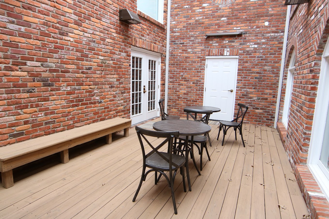 Brick-walled courtyard with tables, chairs, and wood deck