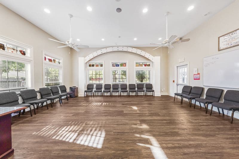 Spacious group therapy room with arranged chairs, hardwood floors, and large windows