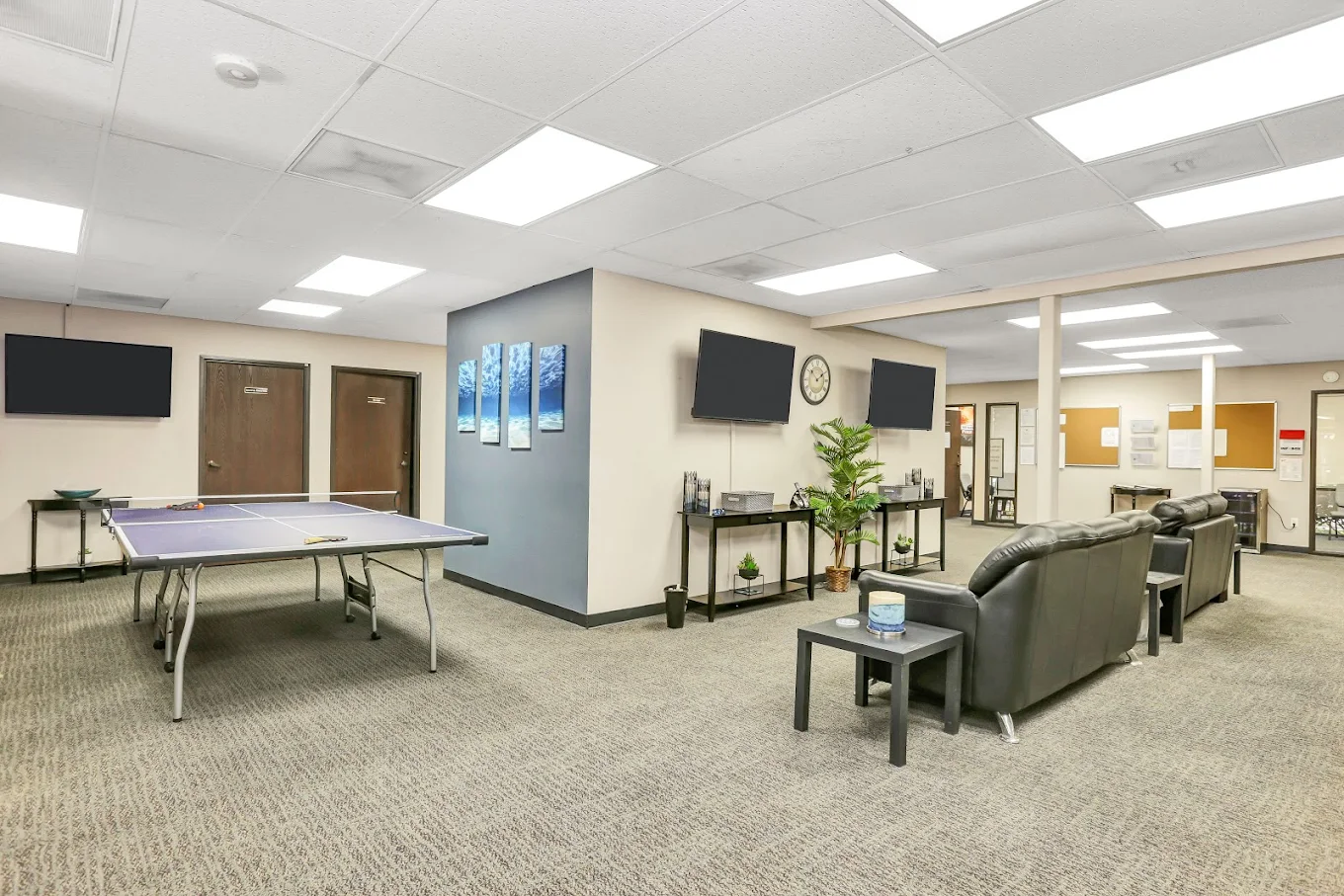 Lounge area with ping pong table, leather couches, and multiple TVs in a treatment facility