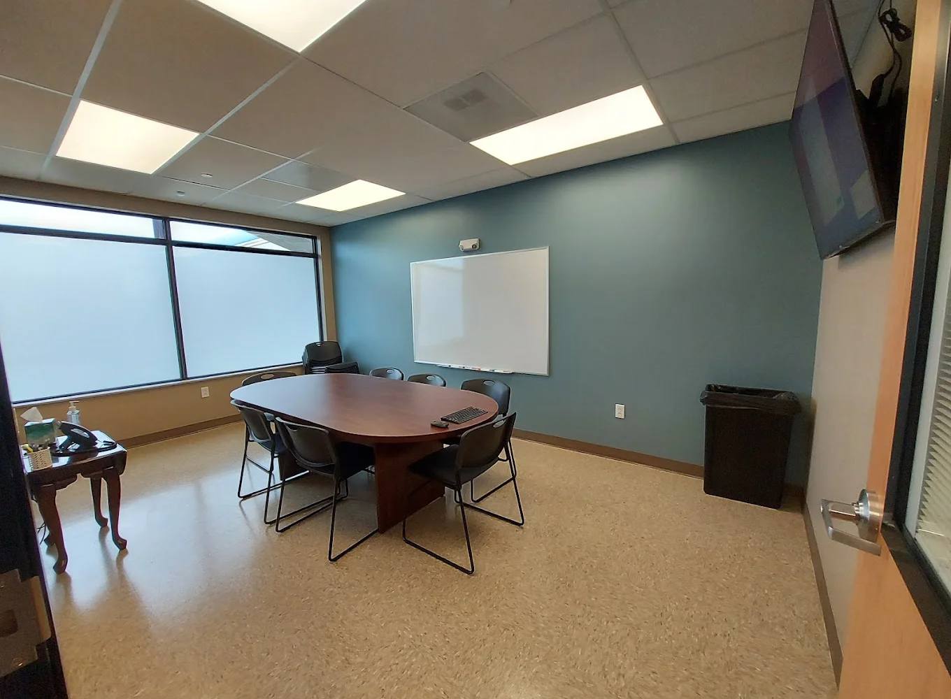Meeting room with oval table, chairs, whiteboard, and TV