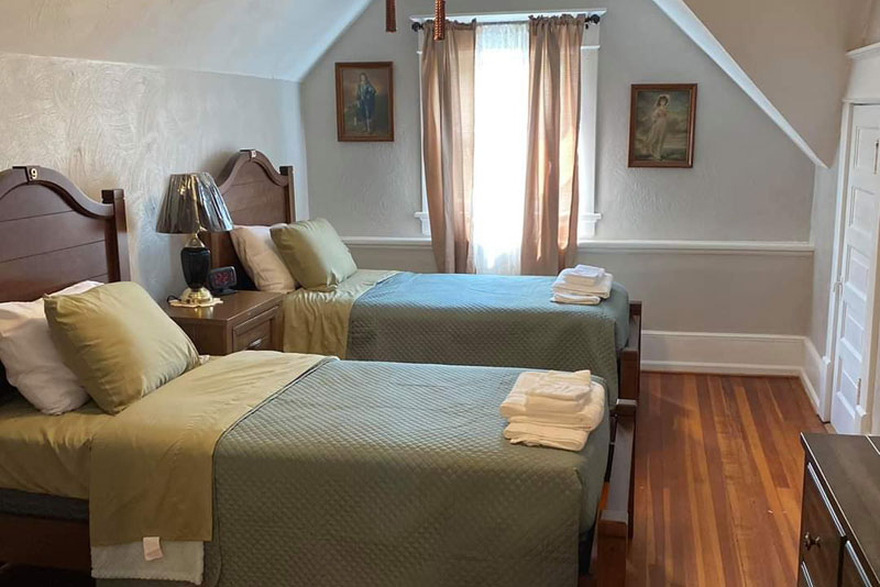 Two twin beds with olive bedding in a sloped ceiling room