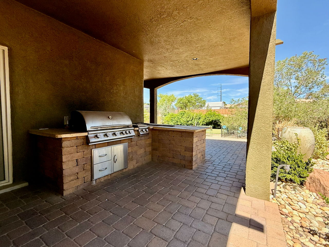 Covered outdoor patio with built-in stainless steel grill, brick counters, and landscaped surroundings
