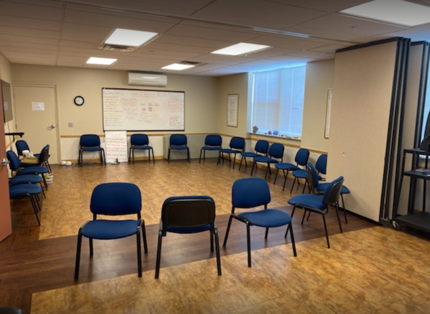 Circle of blue chairs in well-lit group room with whiteboard