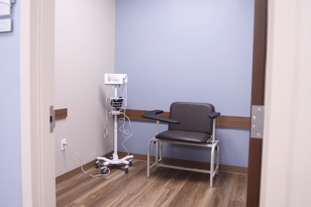BrightView Health treatment room with black patient chairs, landscape artwork, wall-mounted television, blue accent wall, and wood-look flooring