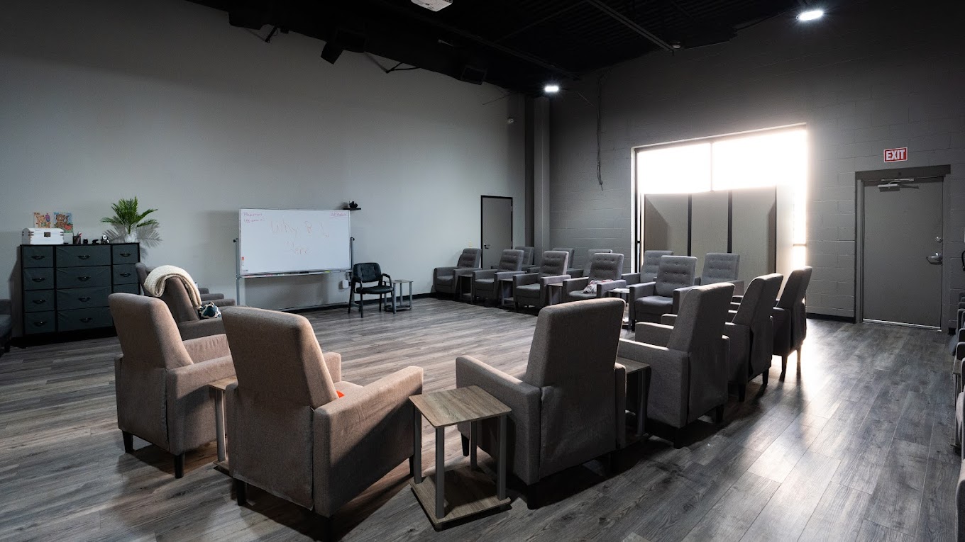 A spacious group therapy room with gray chairs and a whiteboard.