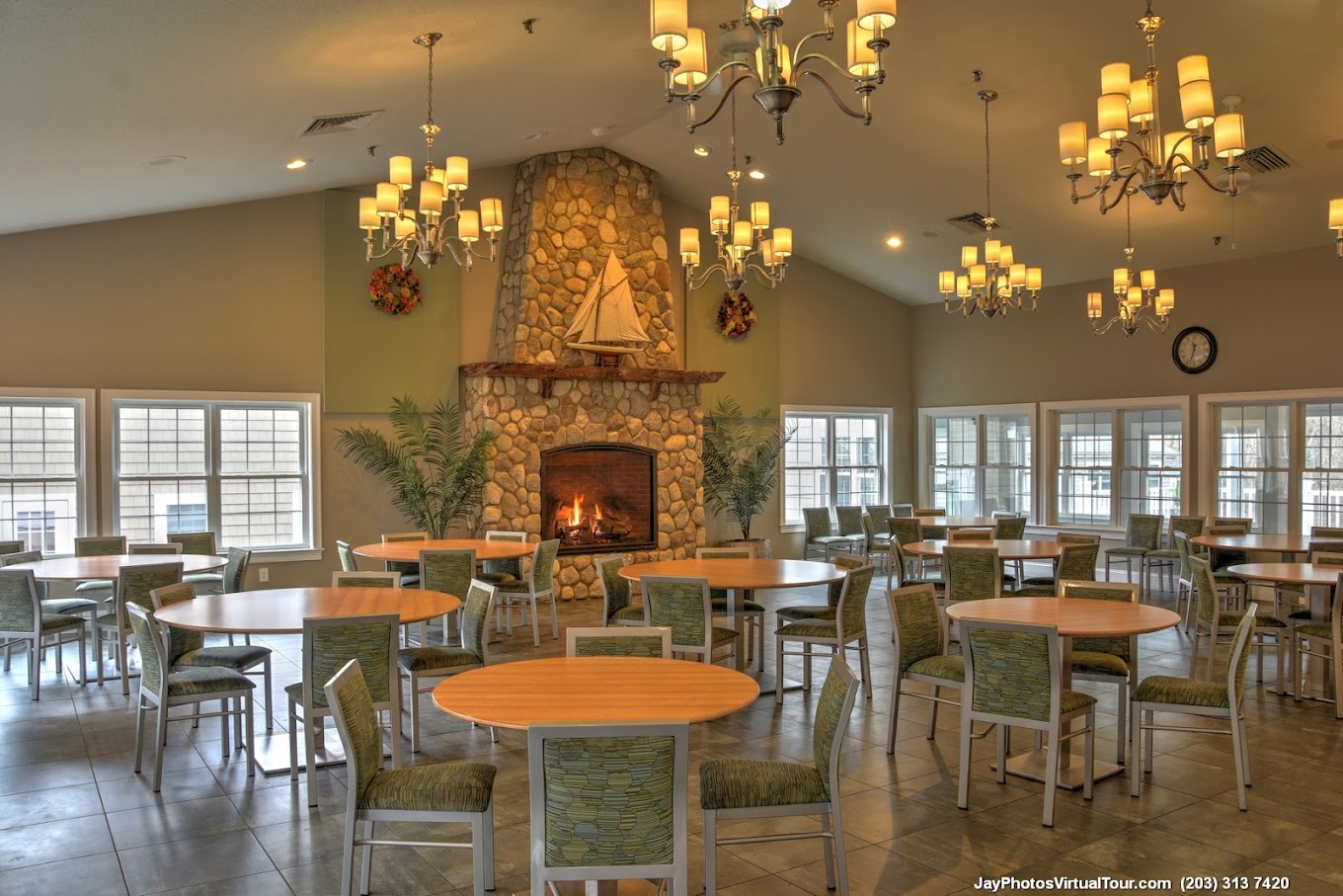 A dining hall with a lit fireplace, round tables, and chandeliers.