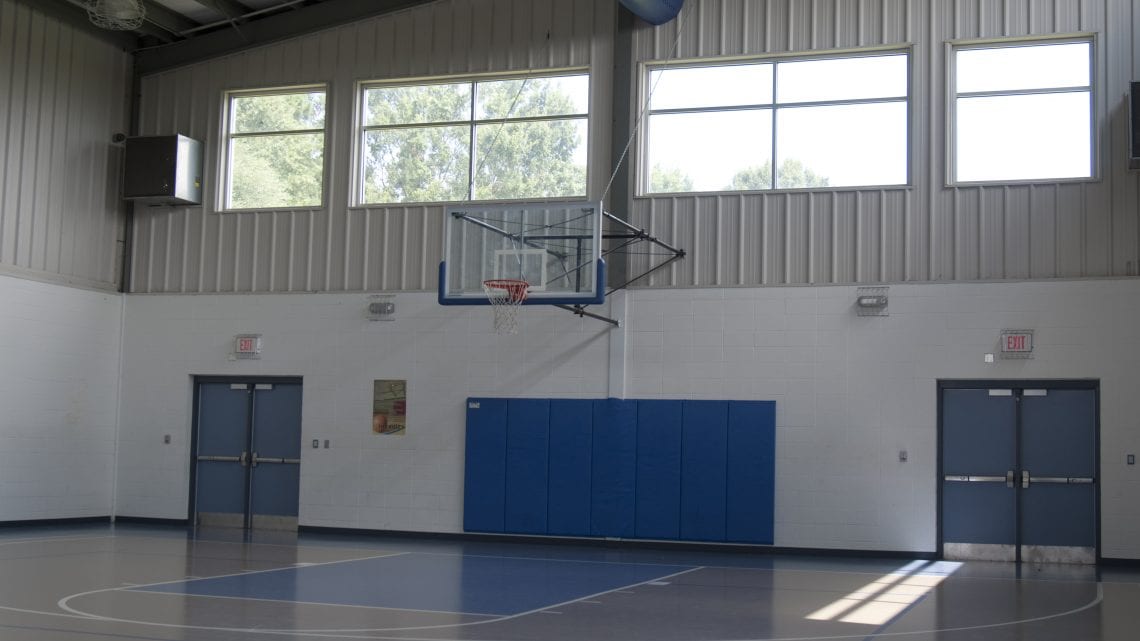 Indoor basketball court with hoop, windows, and padded wall