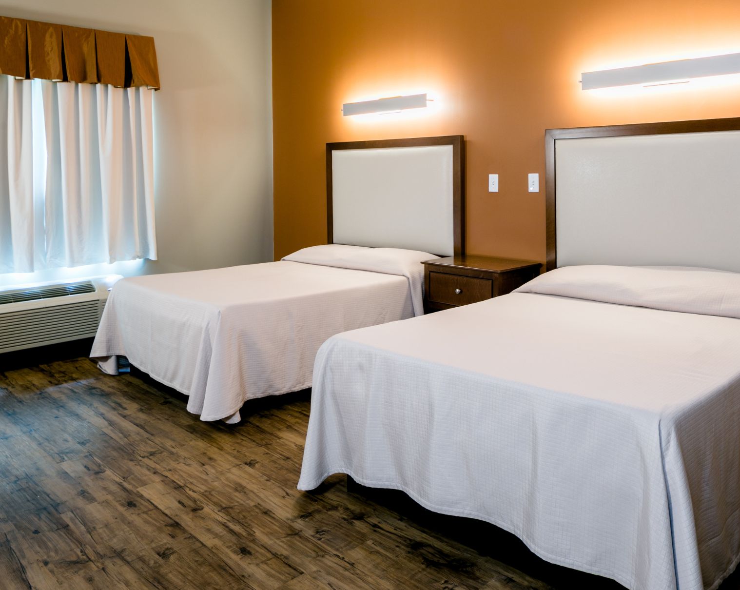 Room with two beds and wood flooring under soft lighting