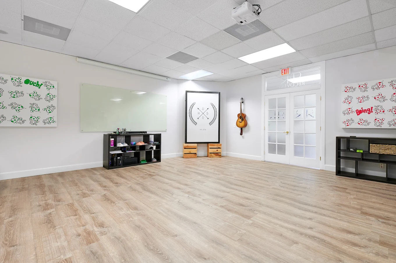 Bright, open therapy room with wooden floors, whiteboard, guitar on the wall, and creative artwork displays