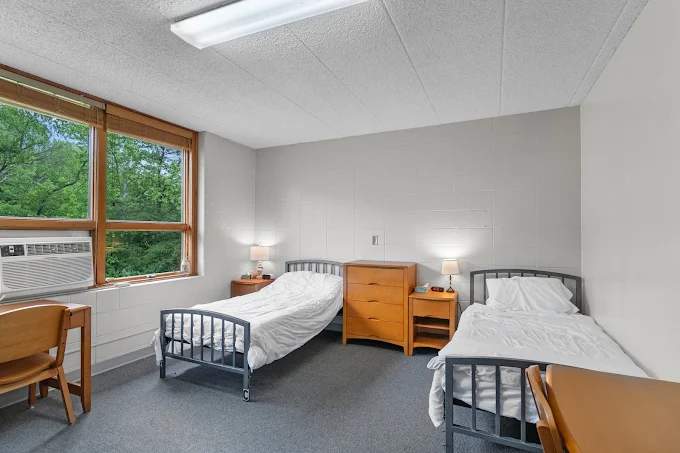Shared bedroom with two twin beds, wooden furniture, and large windows providing natural light.