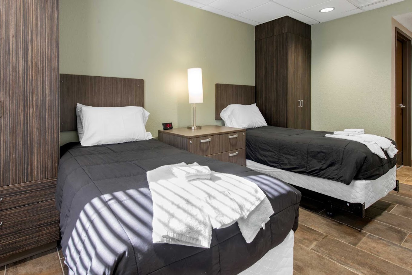 A rehab bedroom with two beds, dark wood furniture, and a bedside lamp.