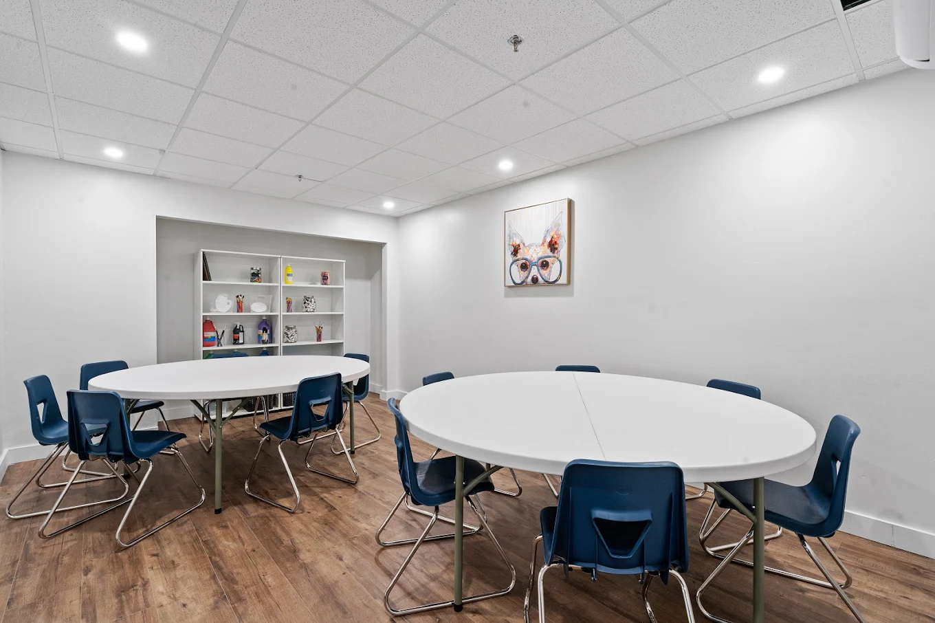 Art therapy space with white walls, round tables, blue chairs, and creative supplies