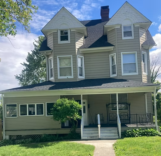 Large tan house with porch, front steps, and green lawn