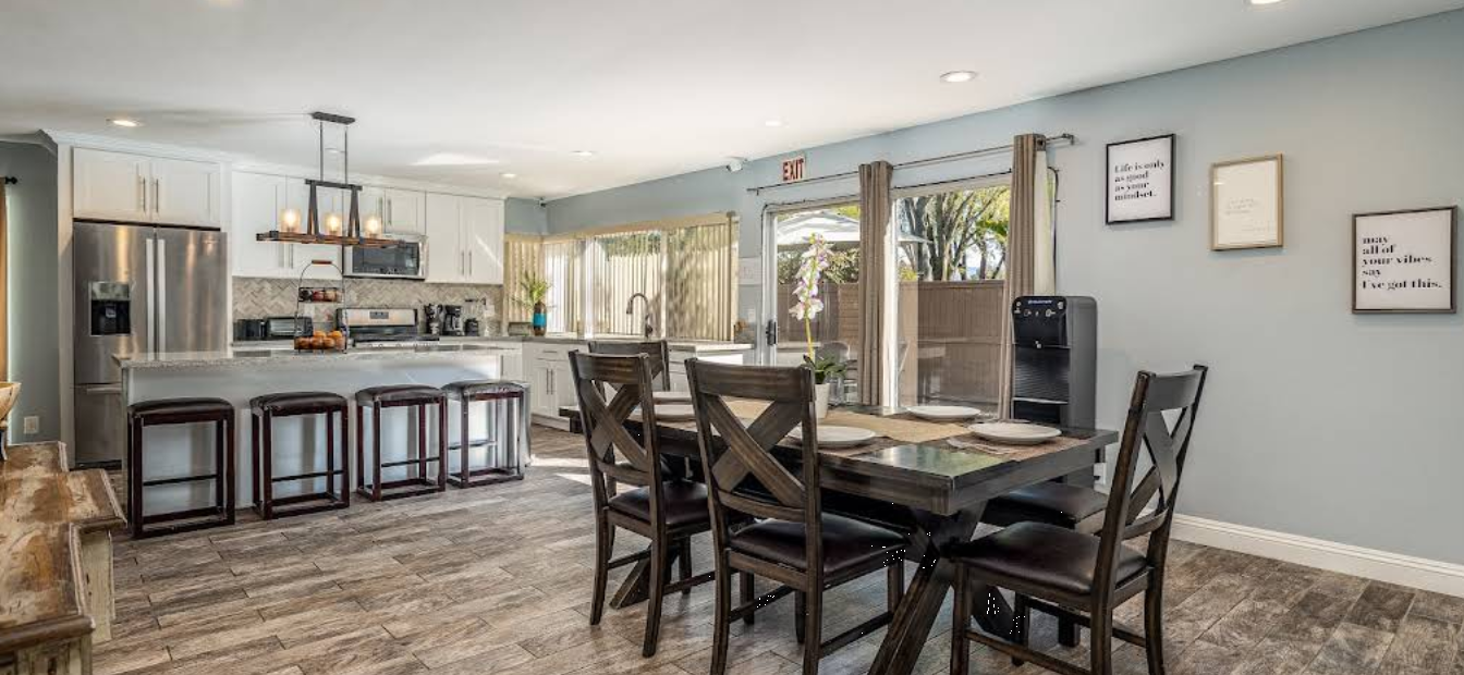 Bright dining area beside open kitchen with large windows and patio access.