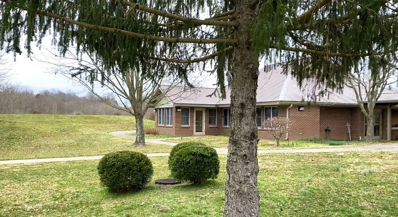 Single-story brick building with grassy lawn, trees, and shrubs