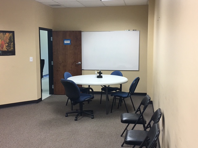 A group meeting room with a round table, chairs, and a whiteboard.