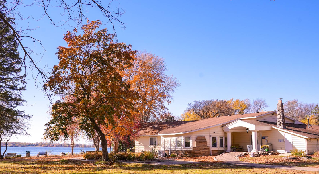 Rehab center exterior by a lake with autumn trees and benches