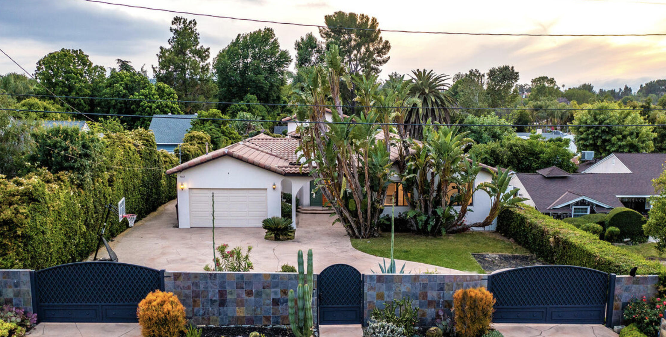 Gated entrance with tropical trees and tile-roof home