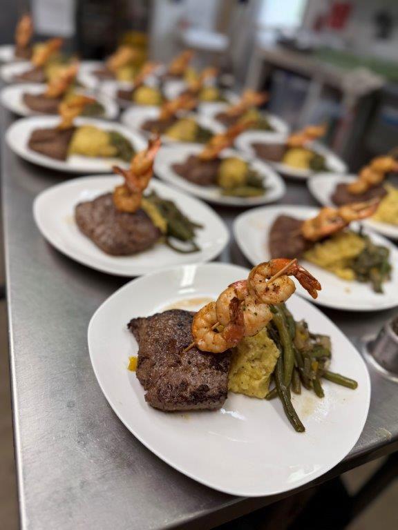 Plates of steak, shrimp, vegetables, and mashed potatoes