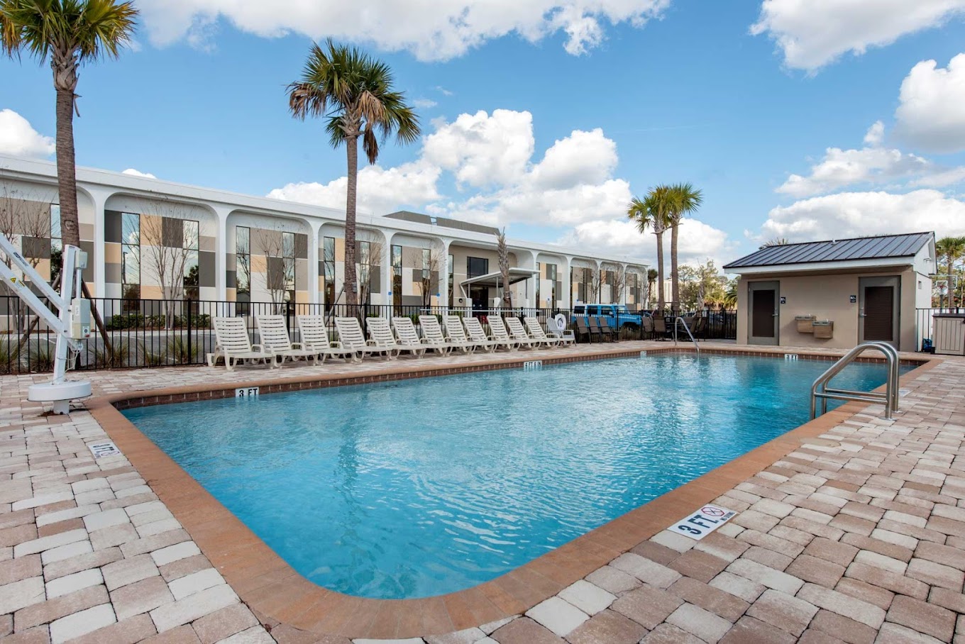 Outdoor pool area with lounge chairs and palm trees under a blue sky.