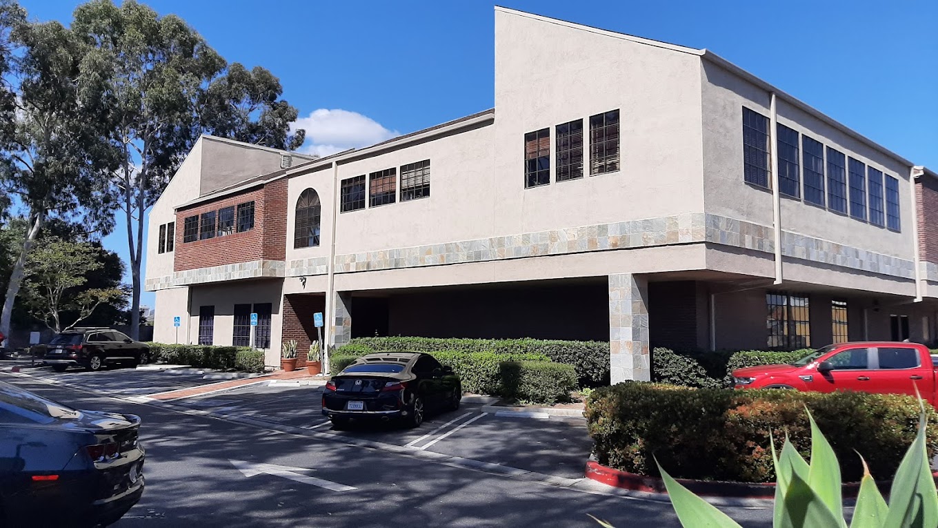 Two-story beige and brick building with parking spaces and greenery.