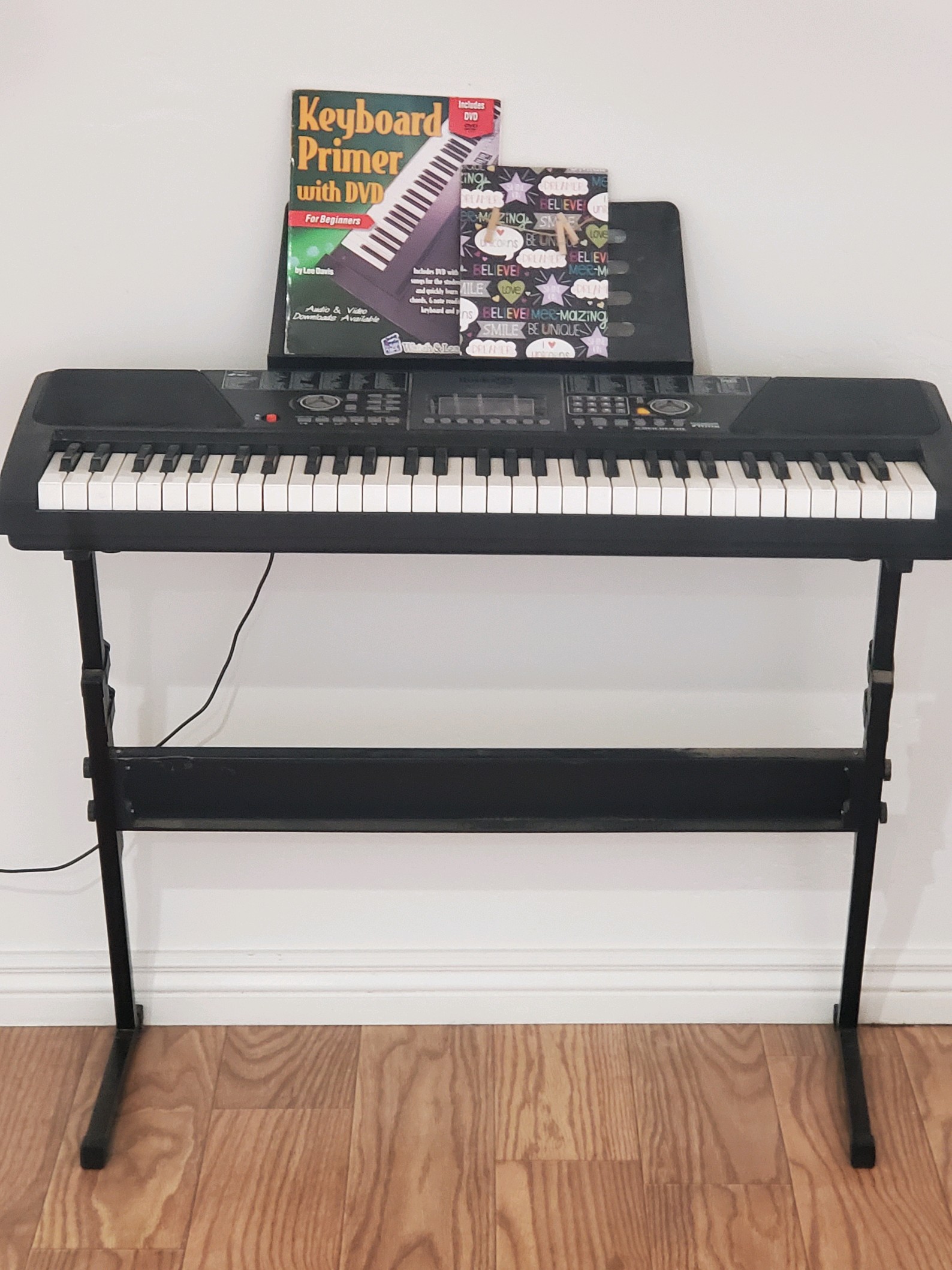 Electric keyboard on stand with a beginner's instruction book and decorative cover, set up for music or recreational use indoors