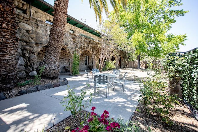 An outdoor patio with tables, chairs, stone walls, and lush greenery.