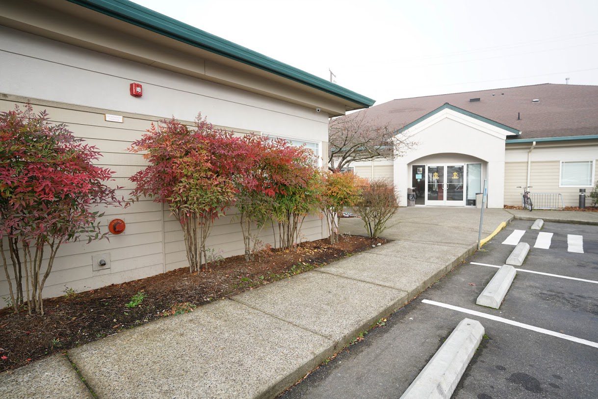 Facility entrance with shrubs, trees, and parking area
