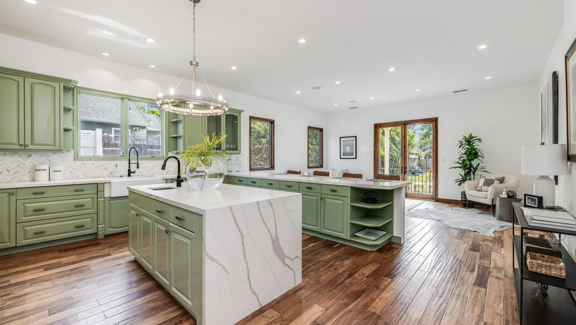 A spacious kitchen with green cabinets and marble countertops.