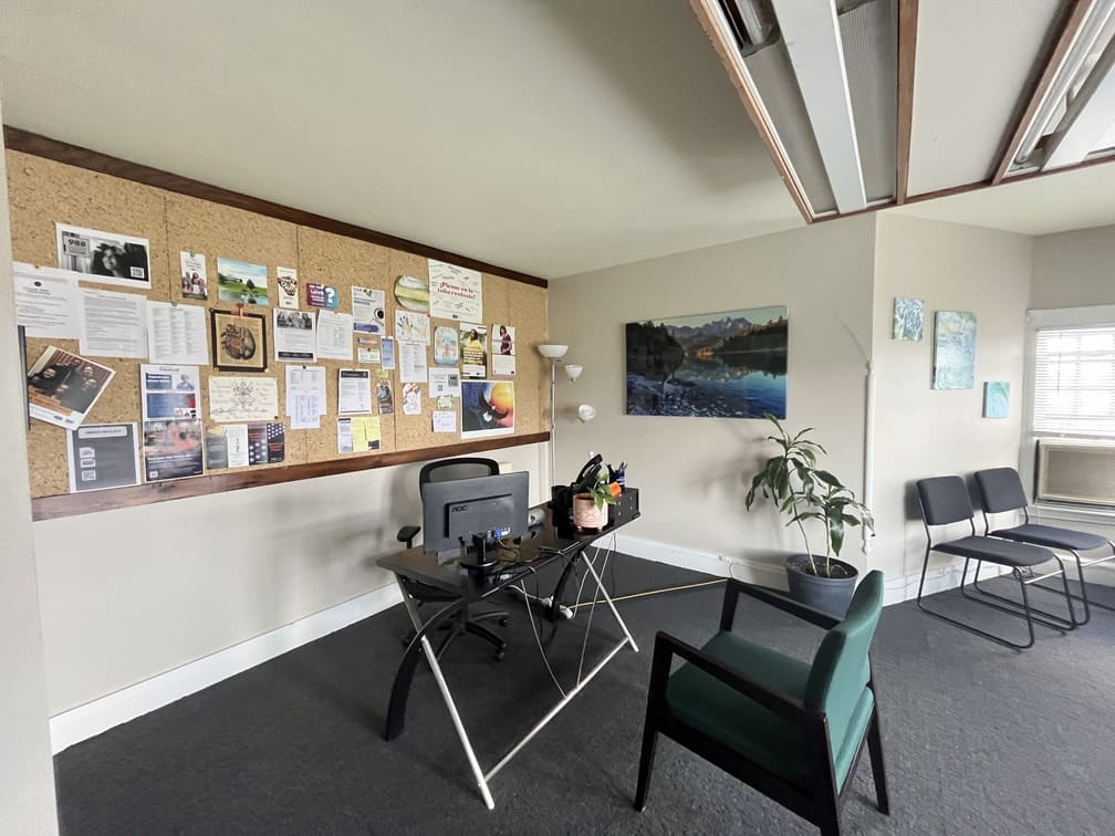 Desk in bright corner office with bulletin board and plants