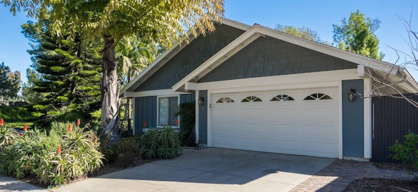 Single-story home with garage surrounded by trees and landscaped plants.