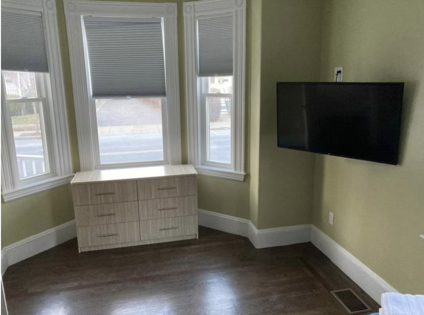 Bay windows with shades, flat-screen TV, and dresser