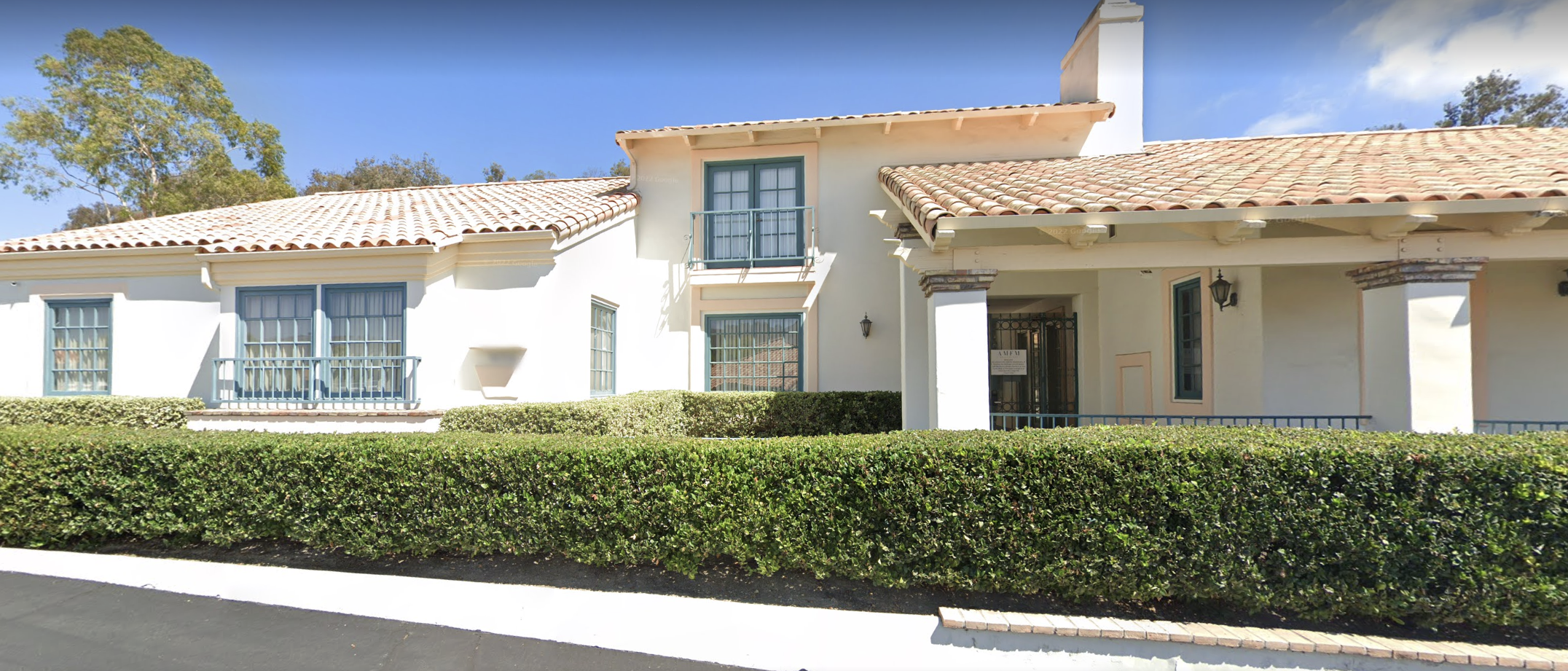 Exterior of a white Spanish-style building with hedges and blue windows.
