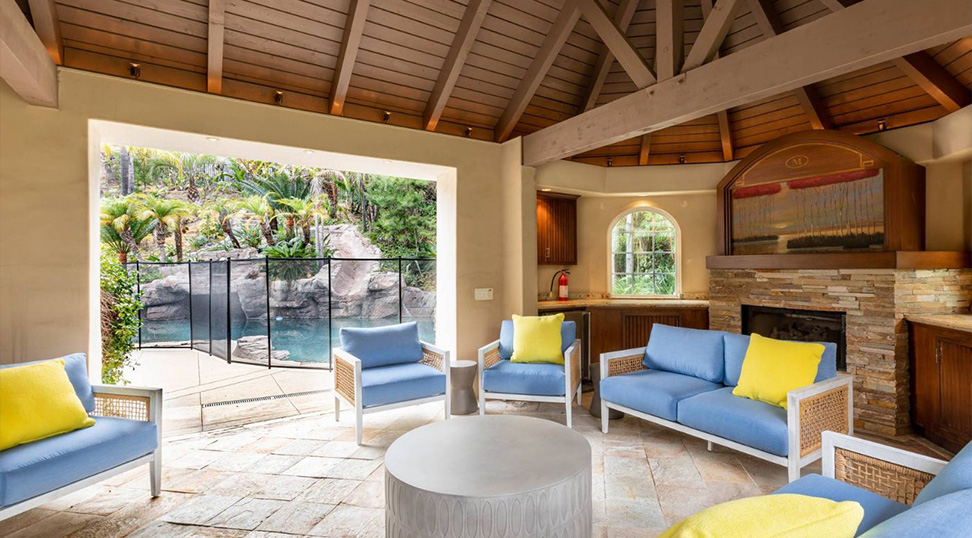 Covered lounge with blue seating overlooking a gated pool area.