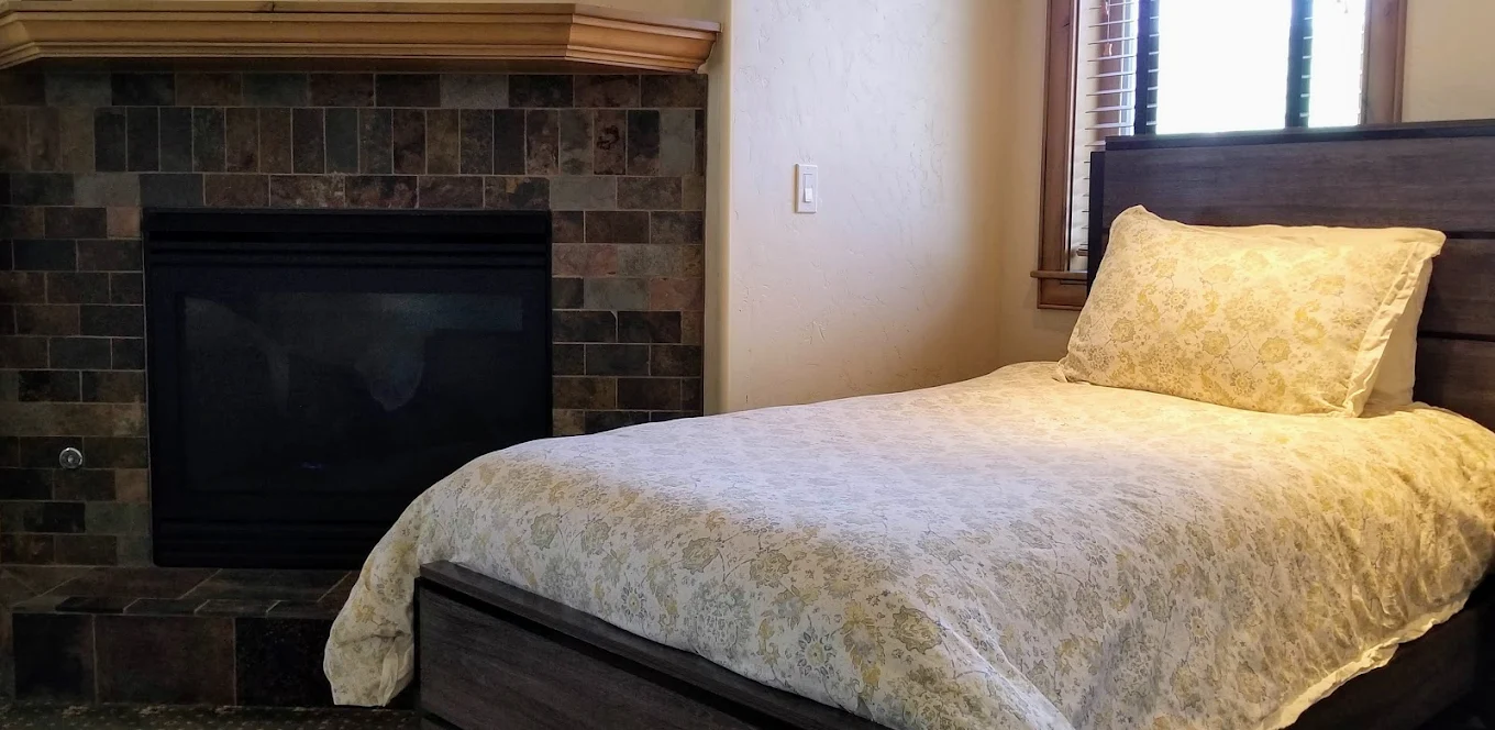Cozy bed next to a tiled fireplace and sunny window