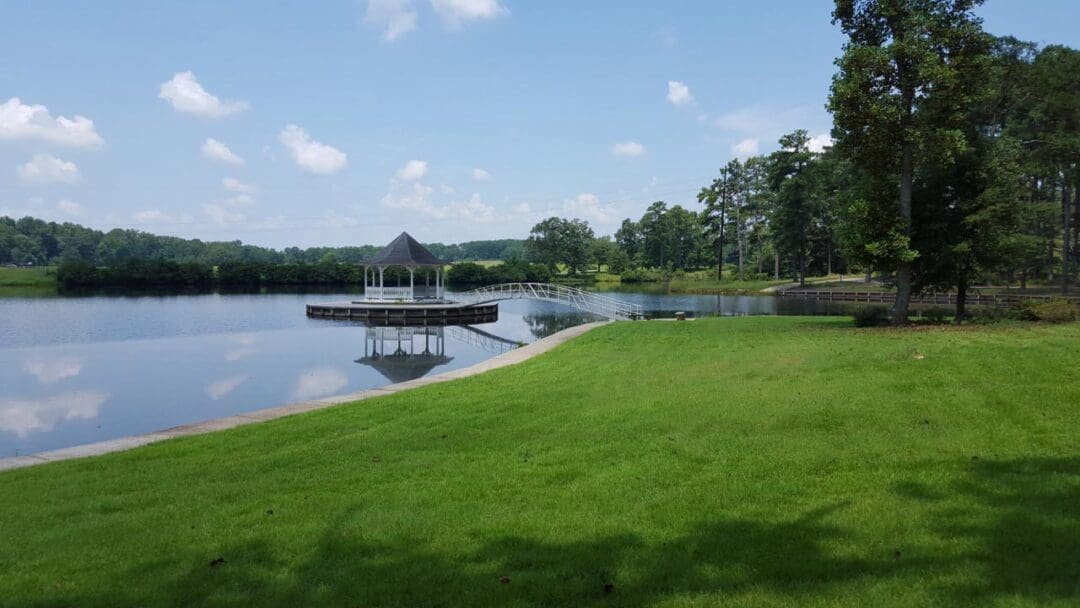 Gazebo on lake with bridge and green grass around