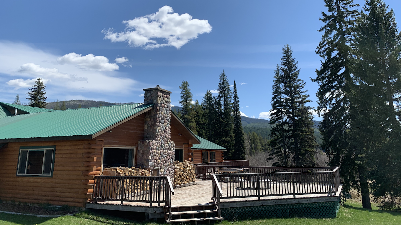 Cabin with chimney and deck surrounded by pine trees