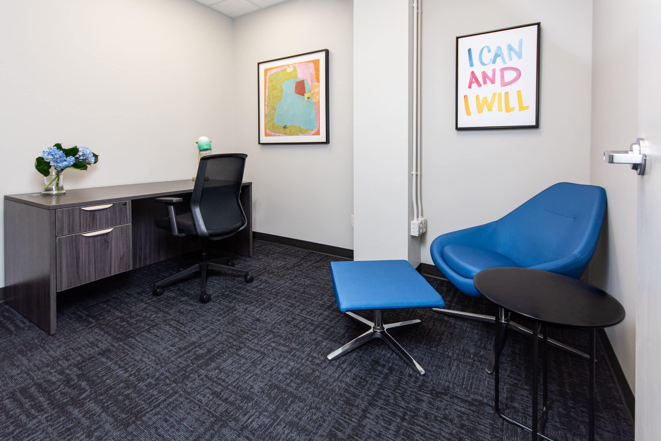 A small office with blue chairs and modern wall art.